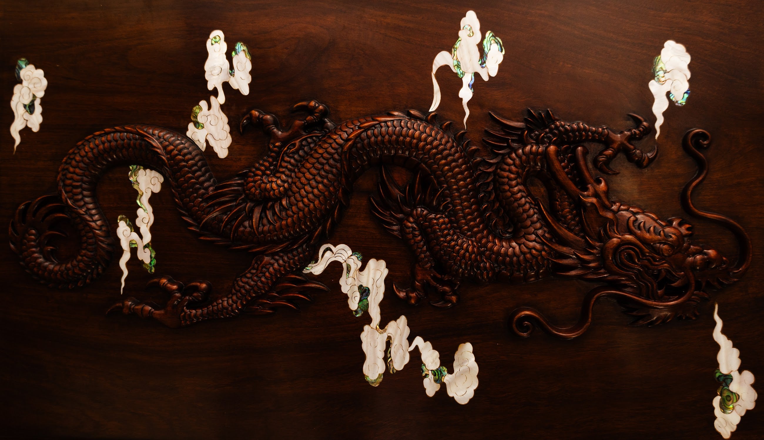 Wooden dragon carving on a dark brown background with pearl inlays